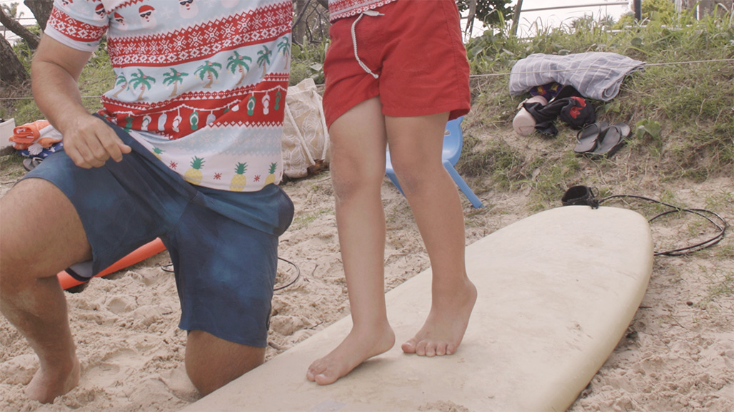 Close up of a boys legs as he stands on a surf board on the sand