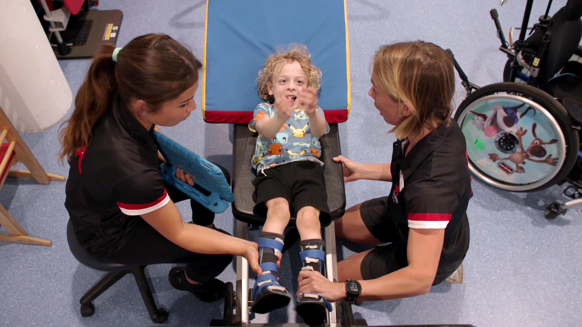 top down view of a boy laying on a pilates reformer bed being assisted by two physiotherapists