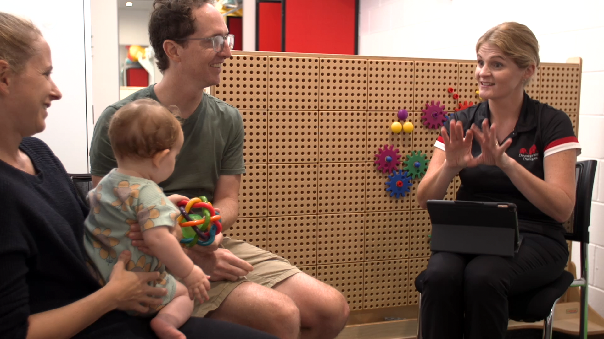 A couple has a toddler sitting on the Mum's lap while they talk to a paediatric physiotherapist